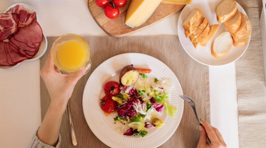 A top-view of a delicious breakfast setting featuring a salad, bread, cheese, tomatoes, and orange juice.